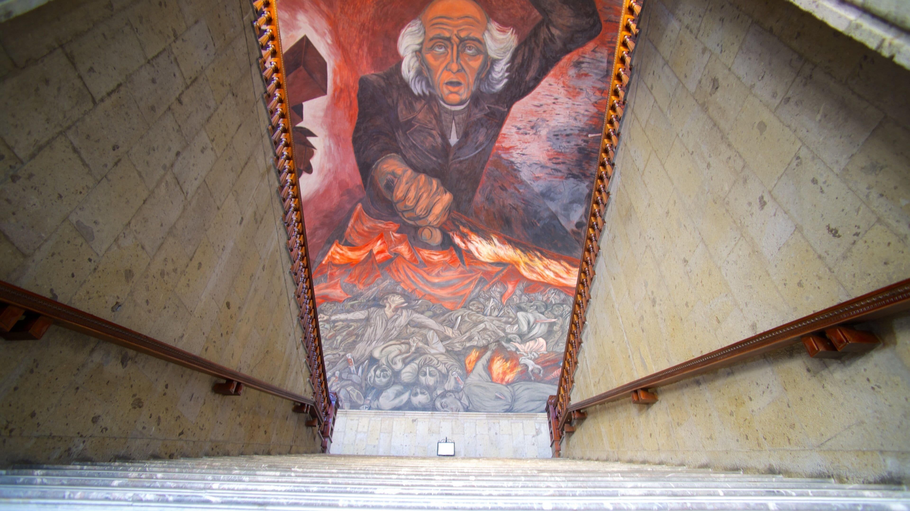 Une fresque représentant une figure avec un bras levé, sur un fond flamboyant, et un escalier menant vers elle.