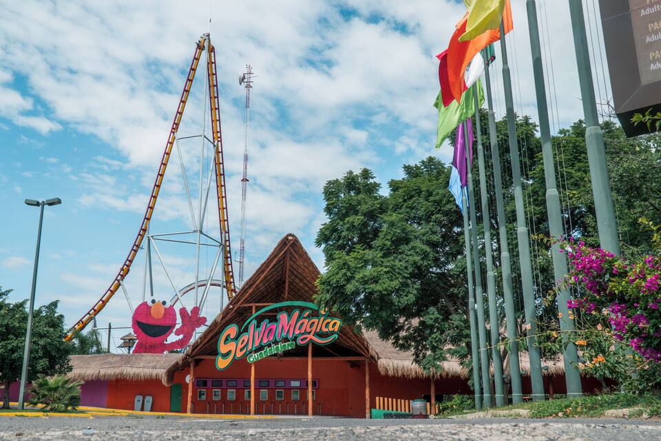 A roller coaster, a building with a thatched roof, and a sign for 'Selva Mágica'.