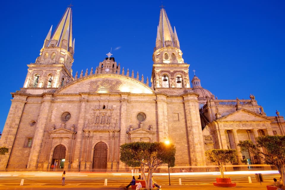 A large cathedral with two tall spires and a dome, surrounded by trees and streetlights.