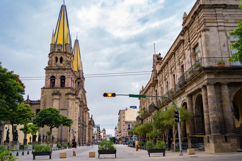 A historic city square with a prominent church spire, classical architecture, and a pedestrian walkway.
