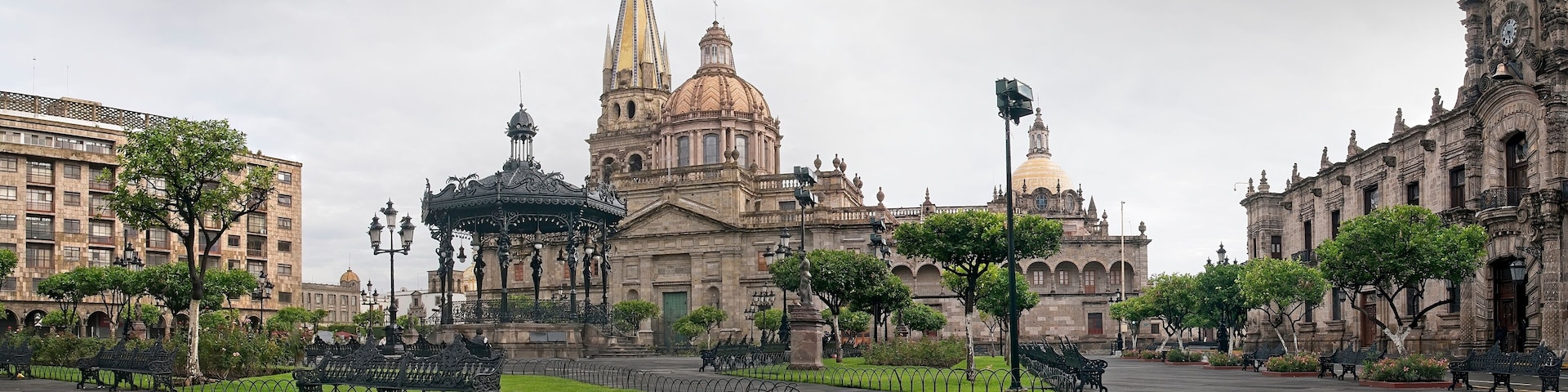 A plaza with ornate buildings, a central fountain, and benches.