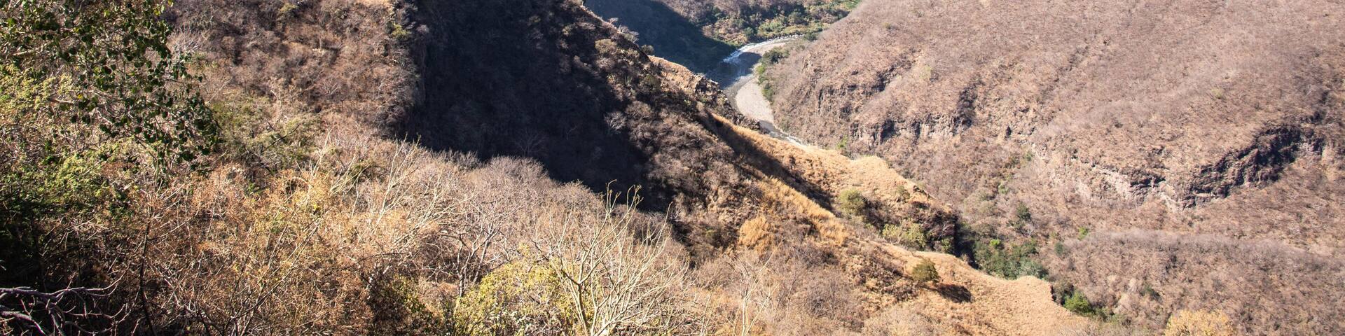 A canyon with a river, dry hills, and distant mountains.