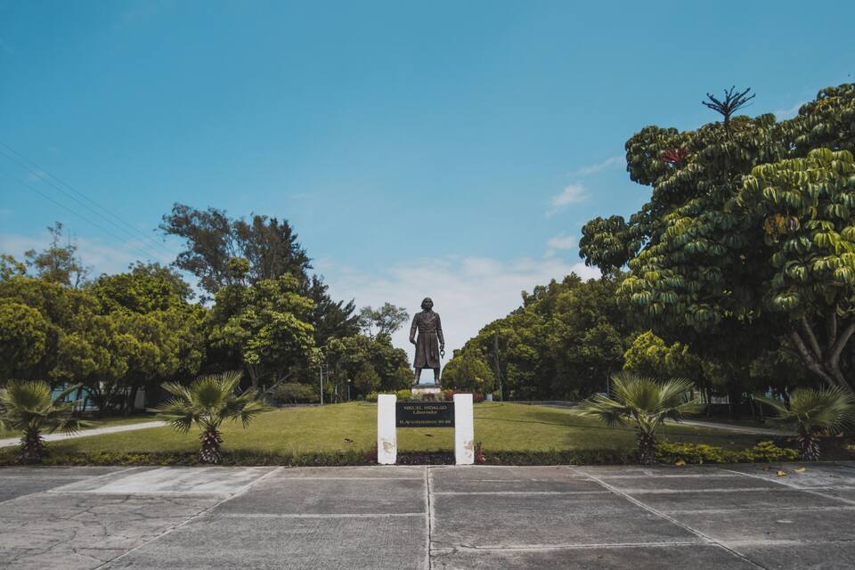 A statue of a historical figure in a park with trees and a clear sky.