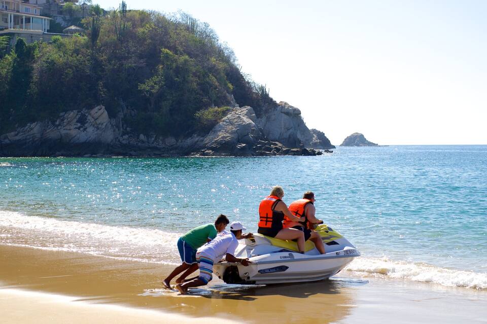 Un jet ski sur une plage, avec des falaises rocheuses en arrière-plan.