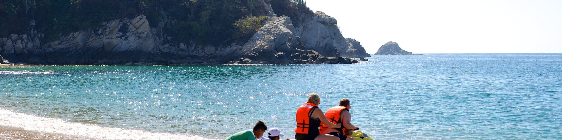 Un jet ski en una playa con acantilados rocosos al fondo.
