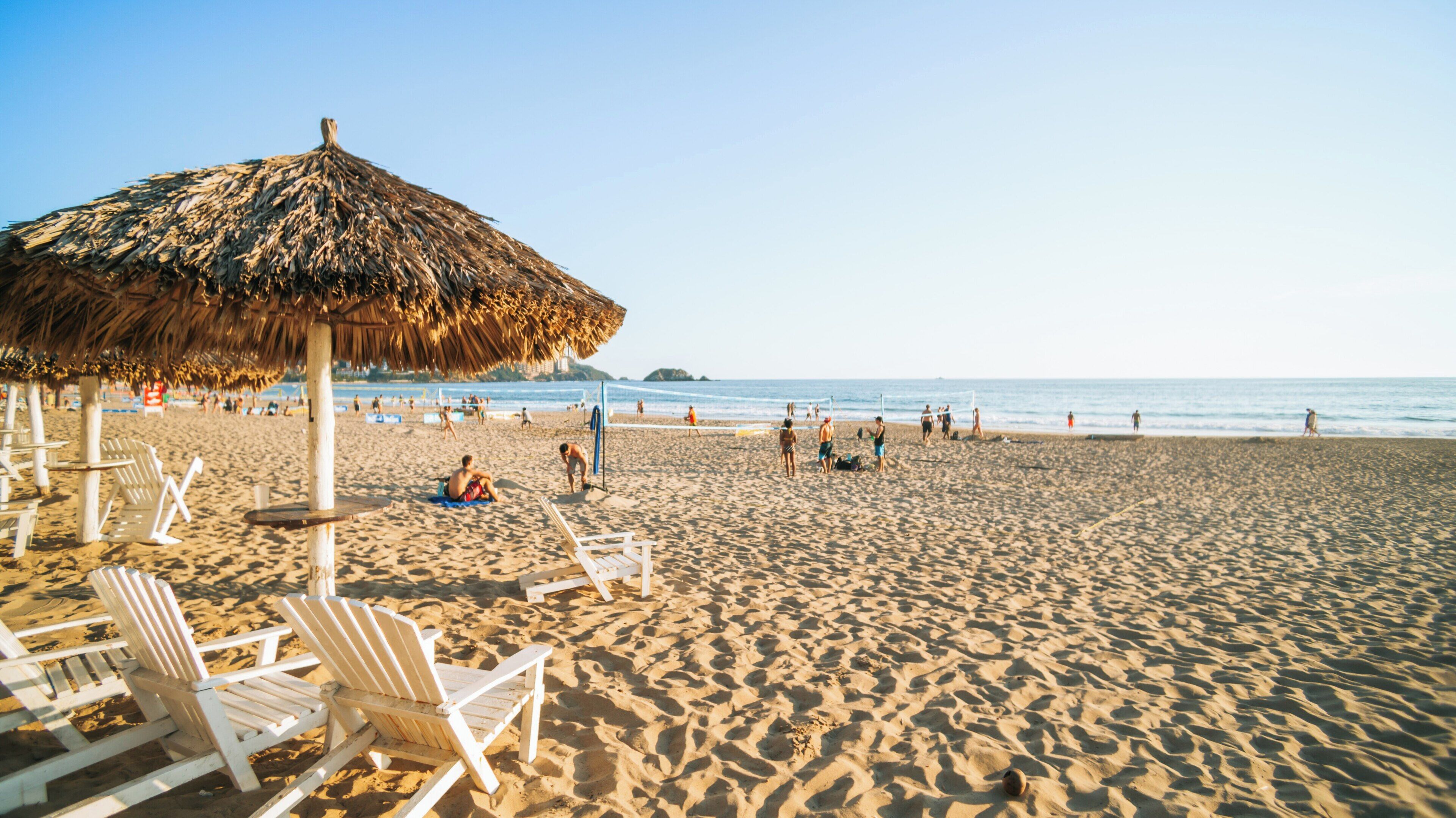 Visitors enjoying a sunny day at El Palmar Beach in Ixtapa Guerrero Mexico with straw umbrellas and lounge chairs lining the sandy shore