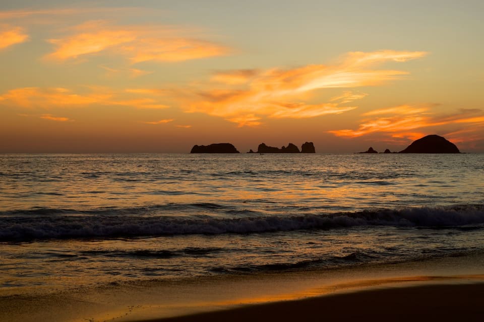 A sunset over a beach with waves and distant rocky islands.