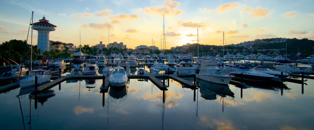 A marina with numerous boats docked, a lighthouse, and a sunset in the background.