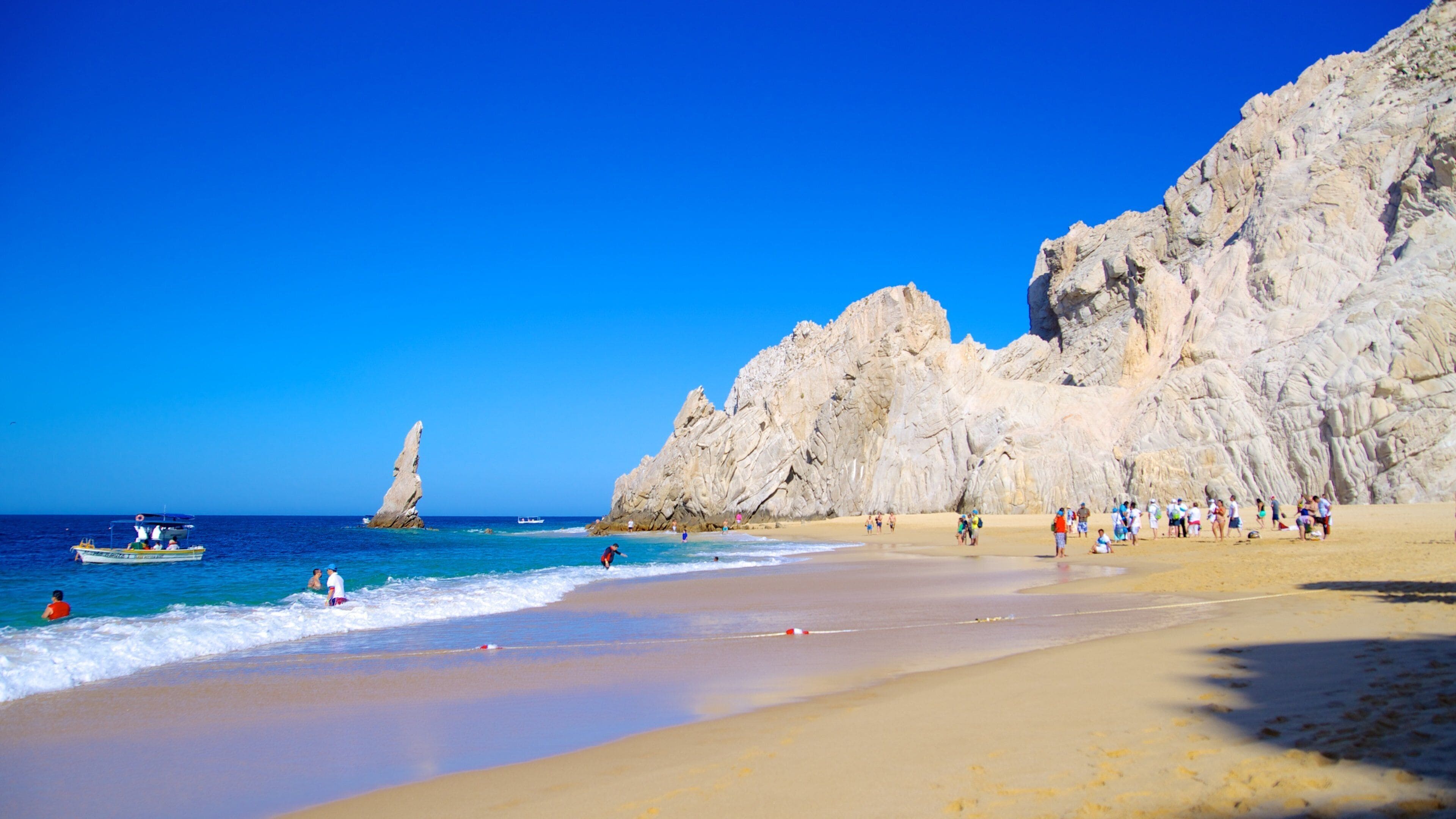 A beach with clear blue waters, rocky cliffs, and a boat in the distance.