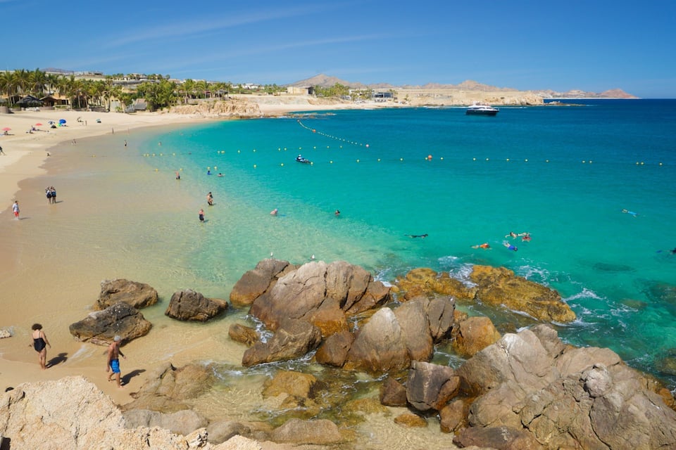 Une plage à l’eau turquoise et limpide, avec une côte rocheuse et un bateau visible au loin.