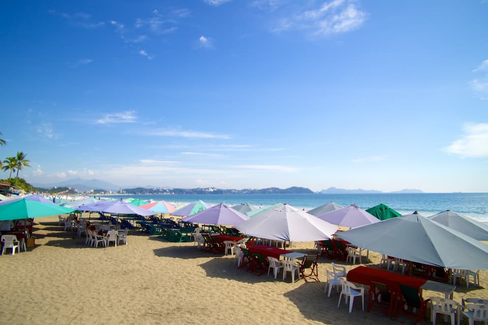 A beach with colorful umbrellas and tables set up for dining.