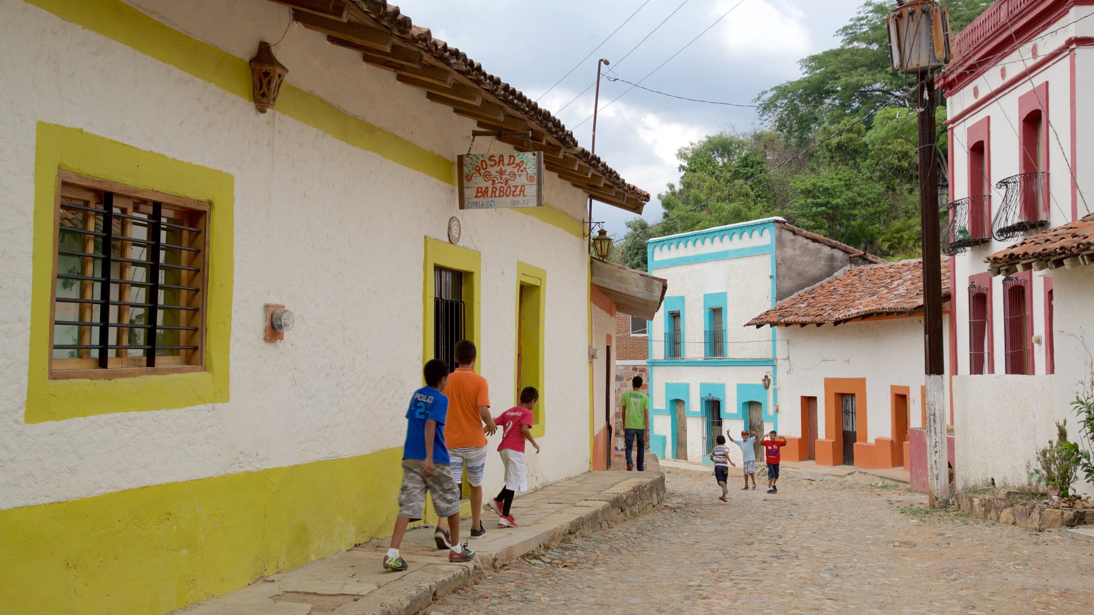 A cobblestone street with colorful buildings, a sign for 'Crosada Barboza', and children playing.