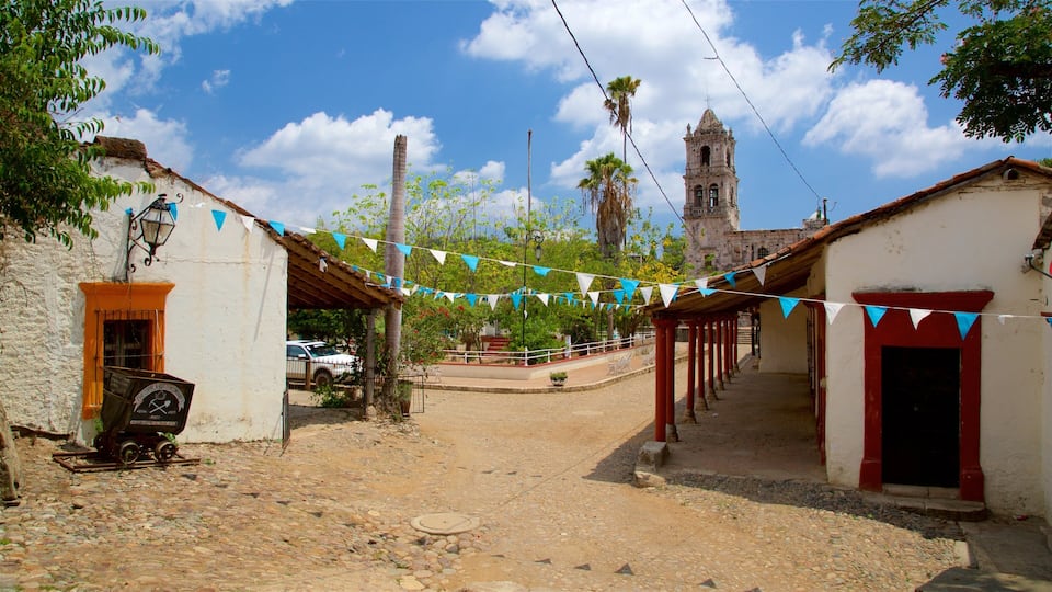 A cobblestone street with buildings, a church tower, and blue and white flags.
