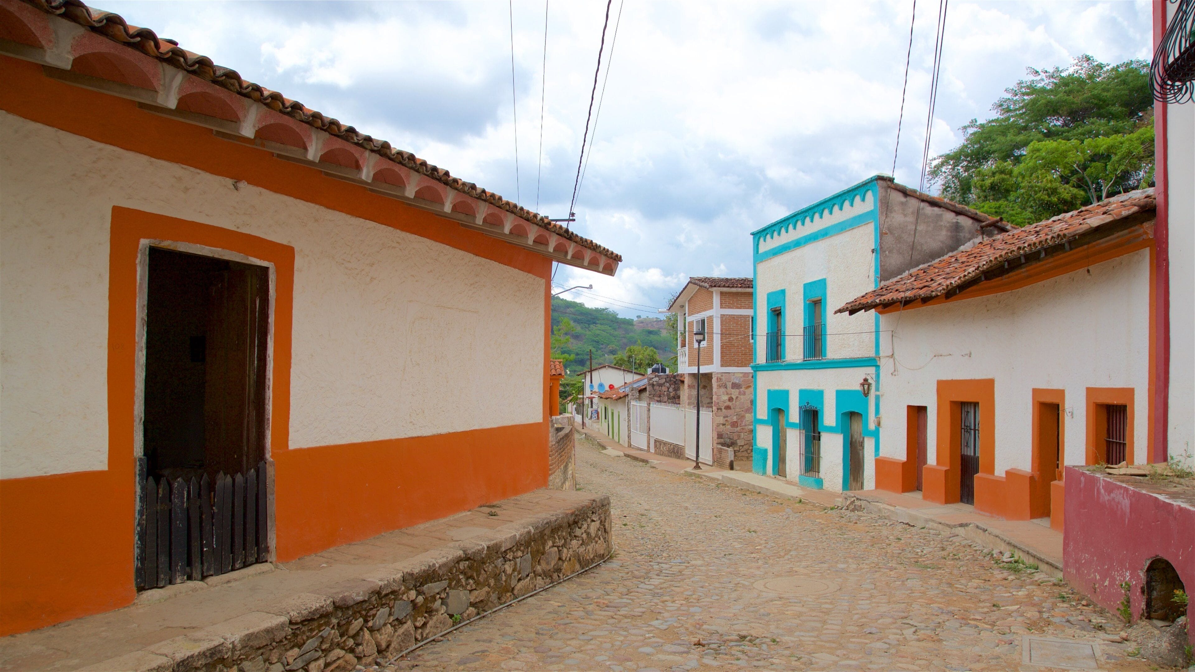 A cobblestone street lined with colorful buildings, a stone wall, and a mountainous backdrop.
