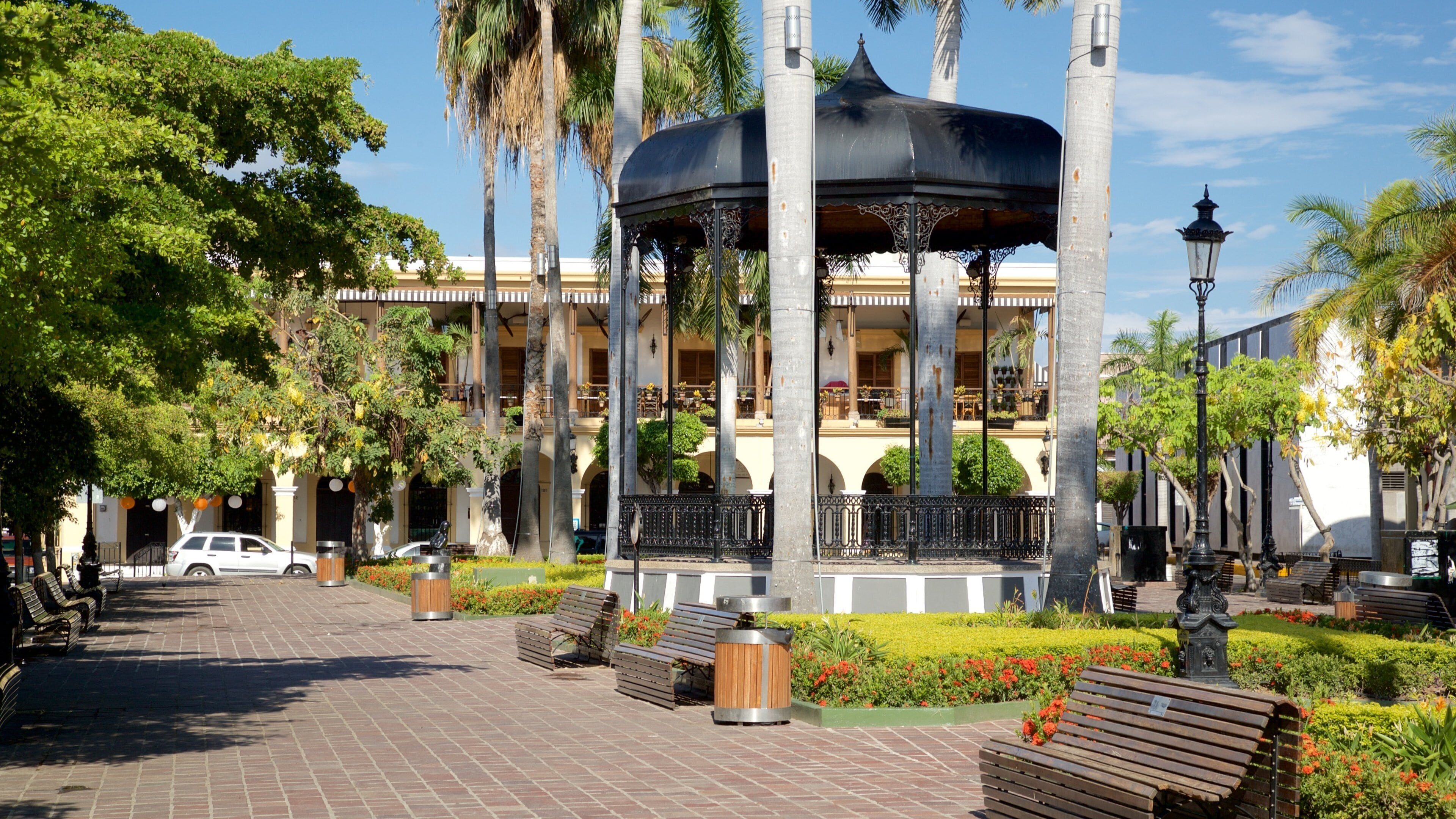 A gazebo with a black roof and columns, surrounded by palm trees and benches.