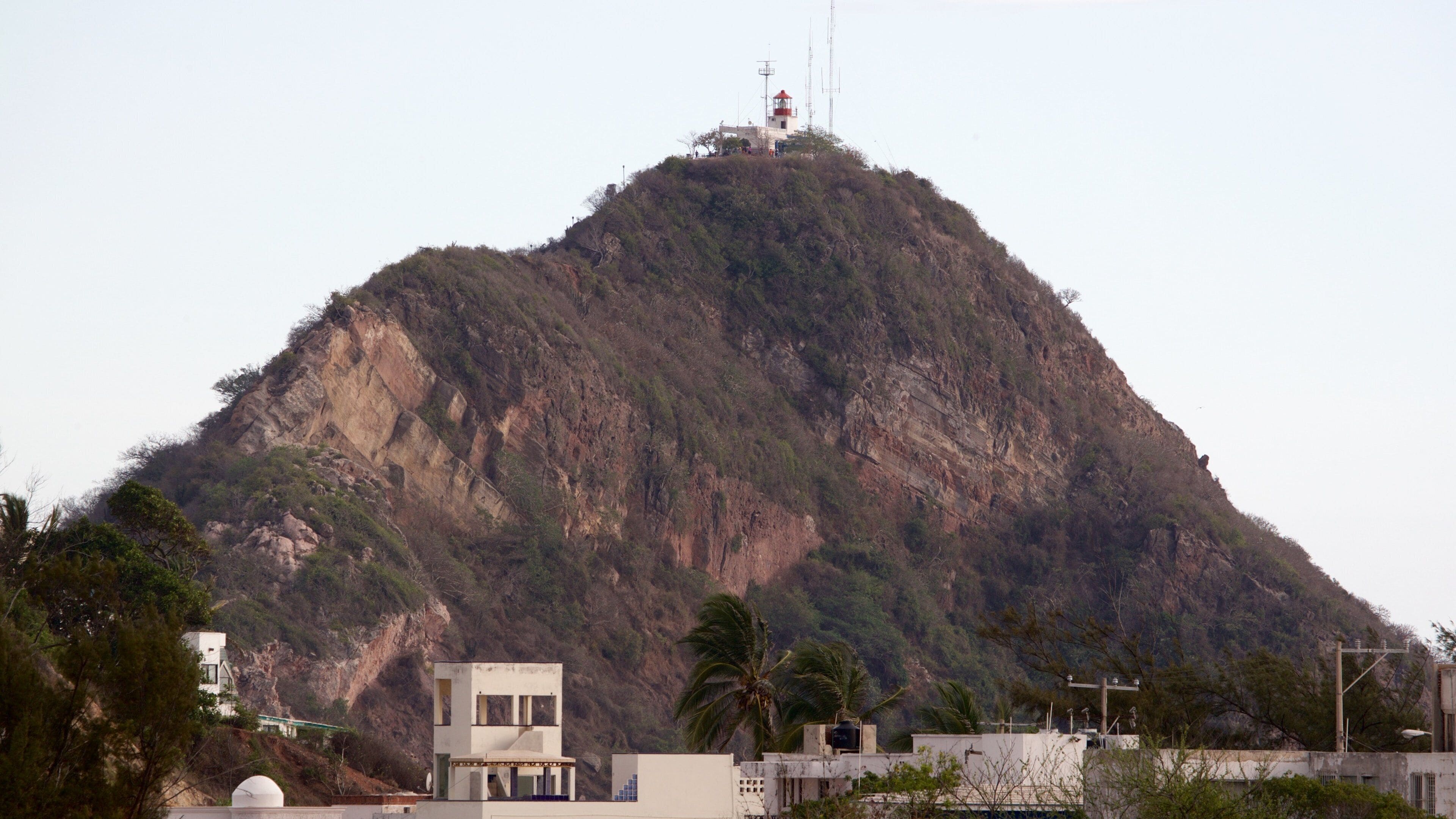 A mountain with a small building on top, surrounded by trees and a few buildings at the base.