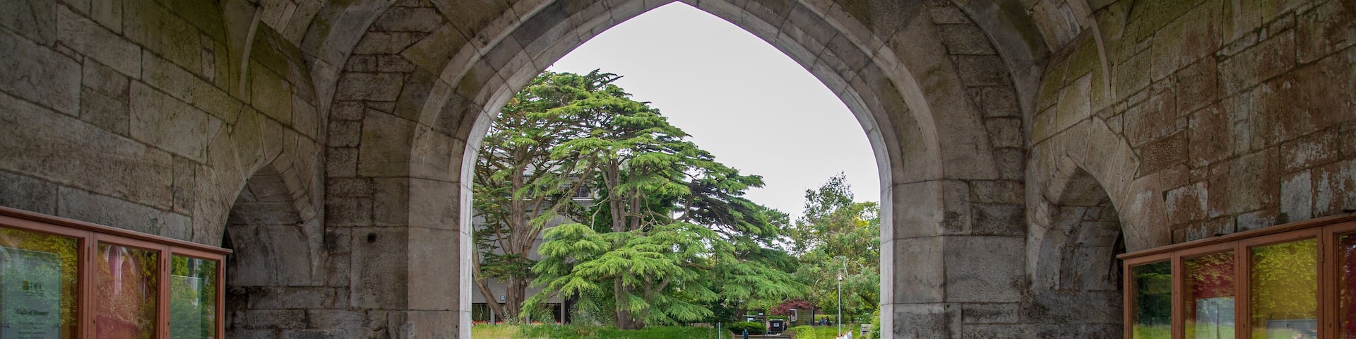 An arched stone corridor with a tiled floor leading to a park.