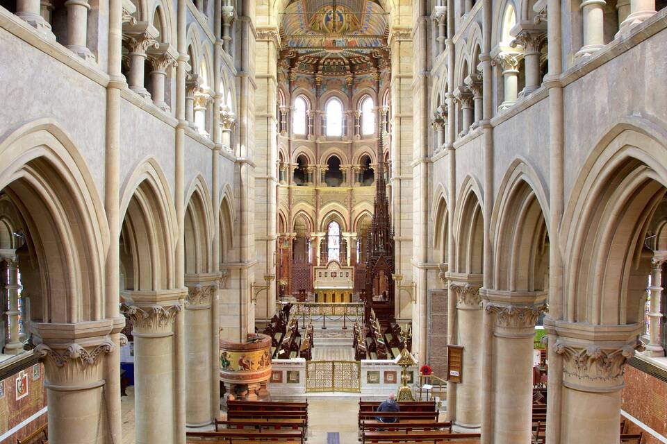 Interior de una catedral con techos abovedados, vidrieras de colores y un altar central.