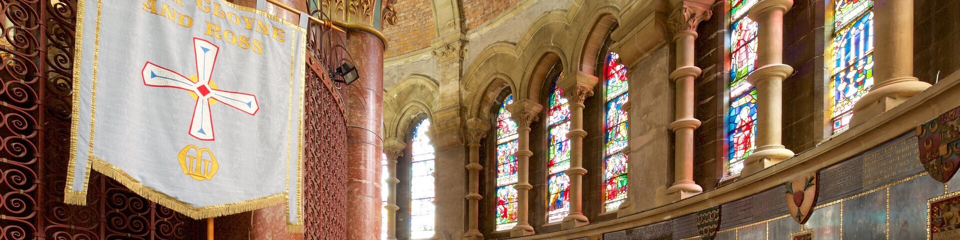 A church interior with stained glass windows, a large cross, and ornate columns.