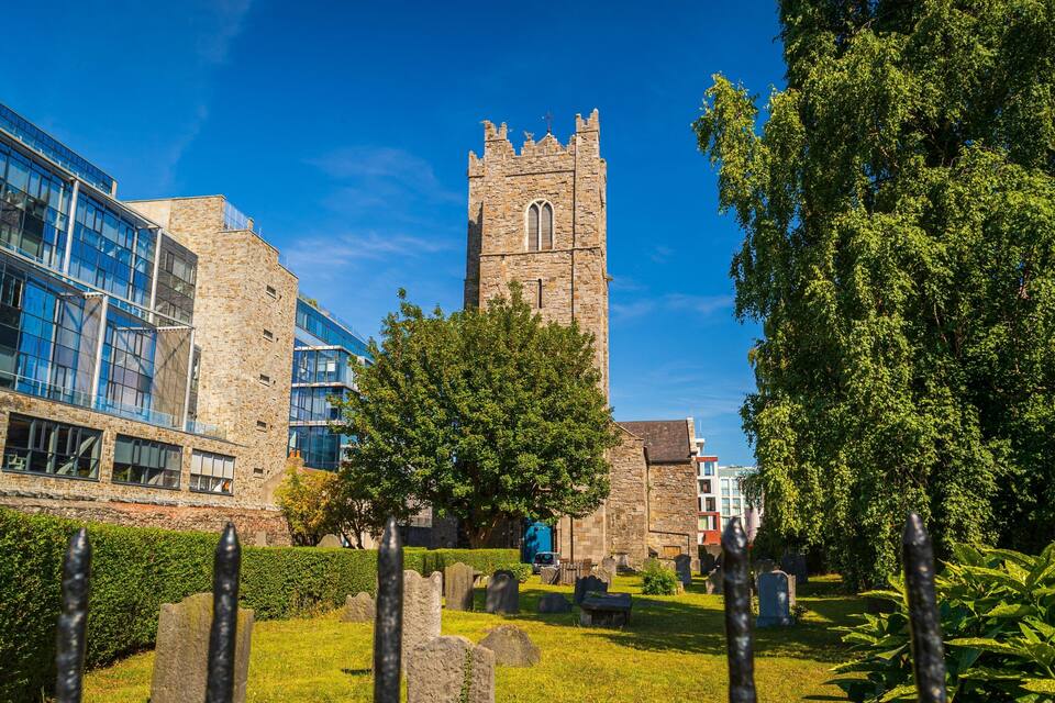A historic church with a tall tower, modern buildings, and a cemetery.