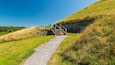 Ein Kiesweg führt zu einer Holztreppe auf einem grasbewachsen Hügel.