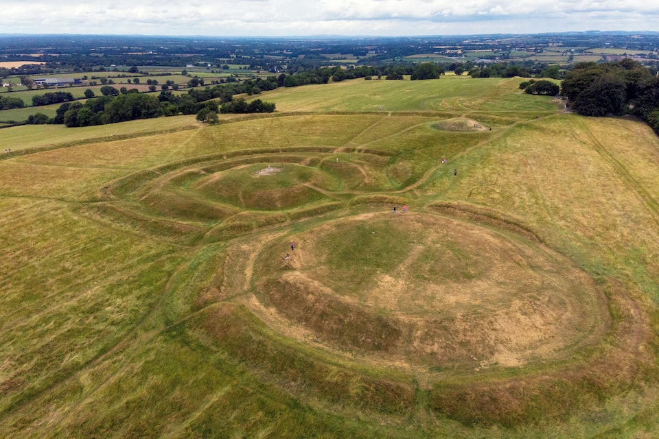 A large, open field with circular mounds and a distant view of a town.