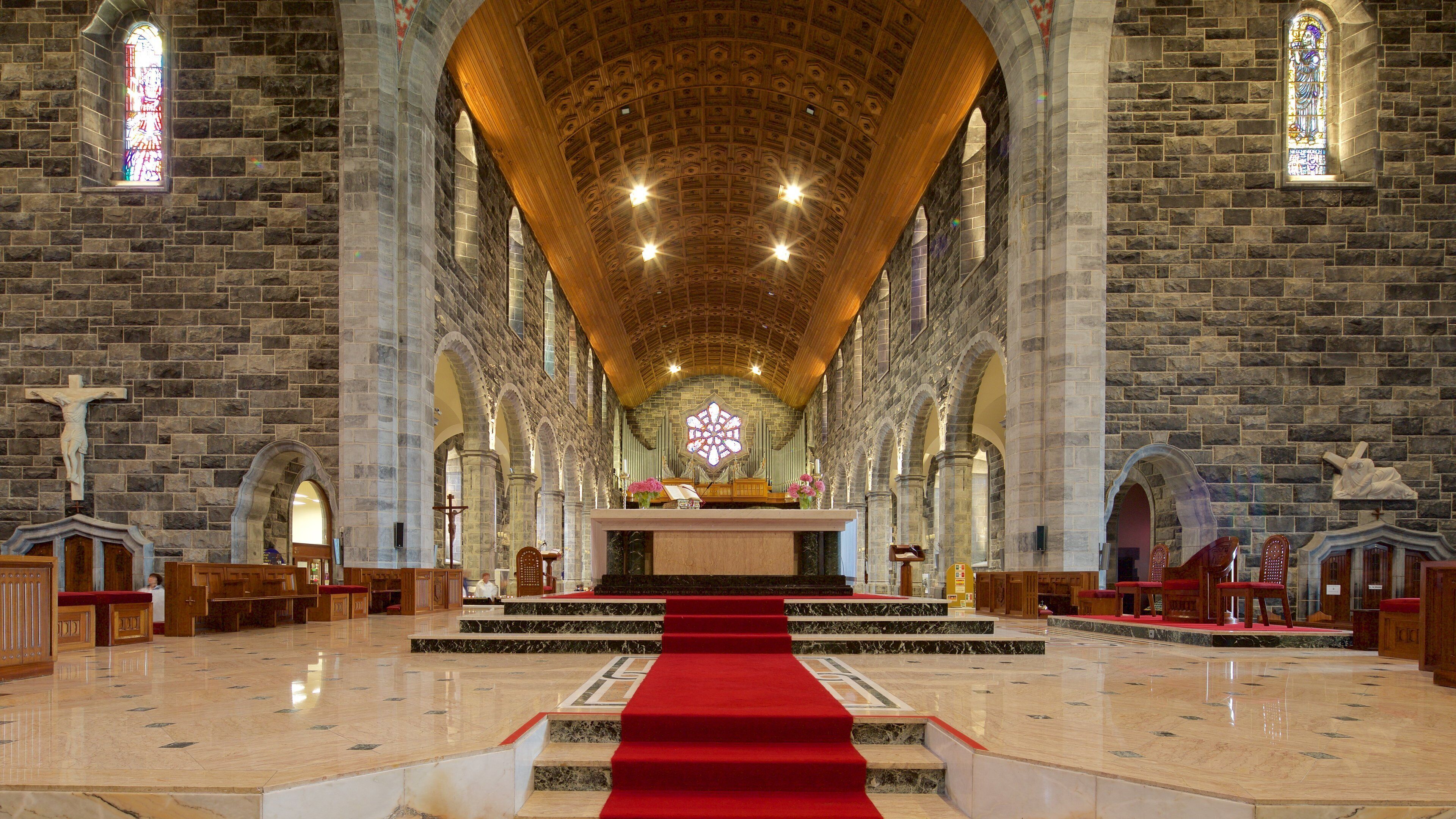 A church interior with stone walls, a wooden ceiling, and a red carpet leading to the altar.