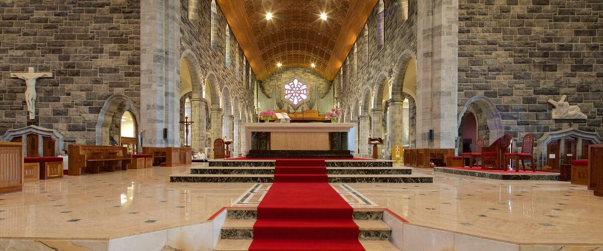 A church interior with stone walls, a wooden ceiling, and a red carpet leading to the altar.