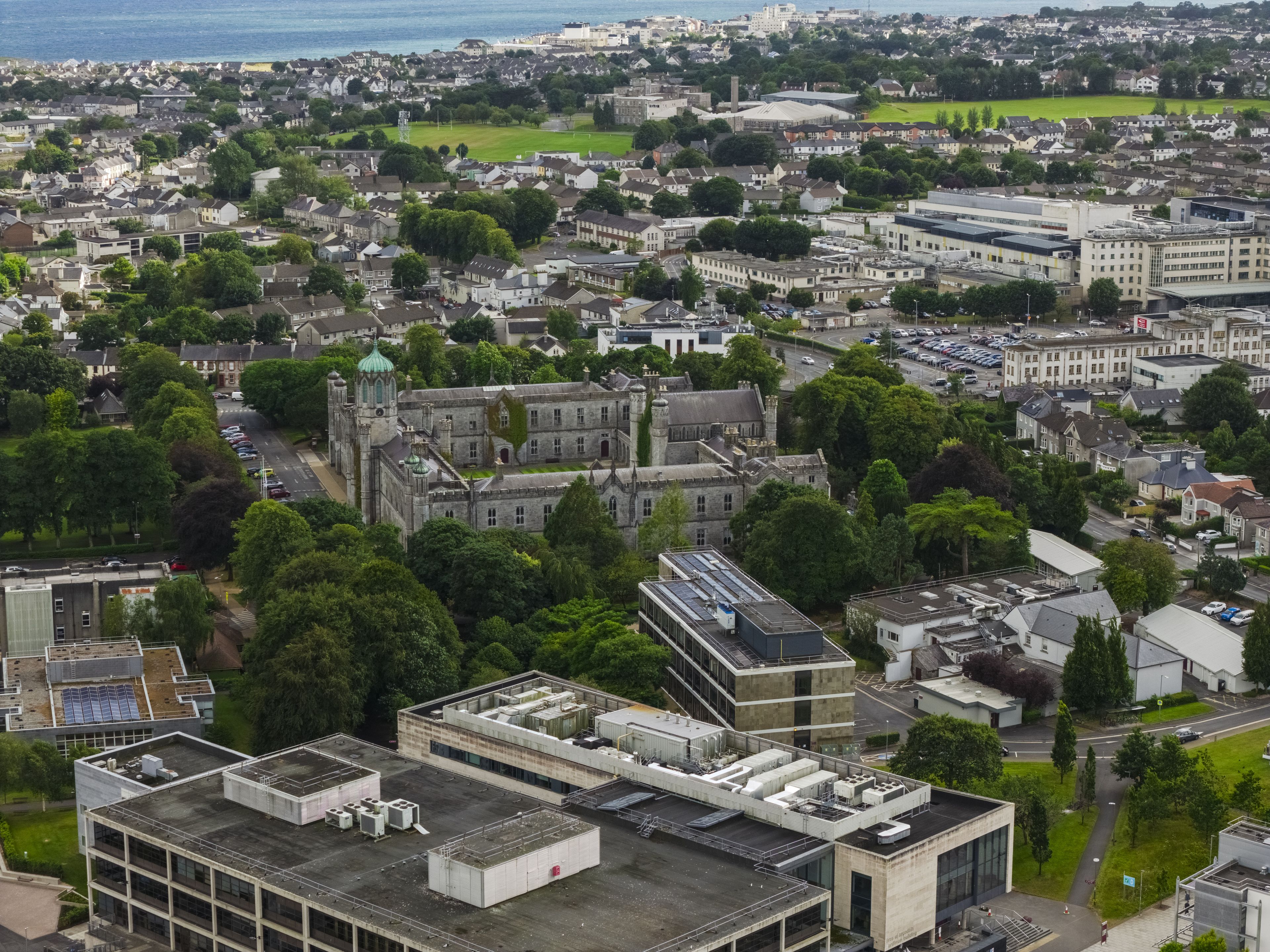 Aerial view of the University of Galway campus featuring historic stone architecture surrounded by lush green trees and modern buildings in Galway, County Galway, Ireland.