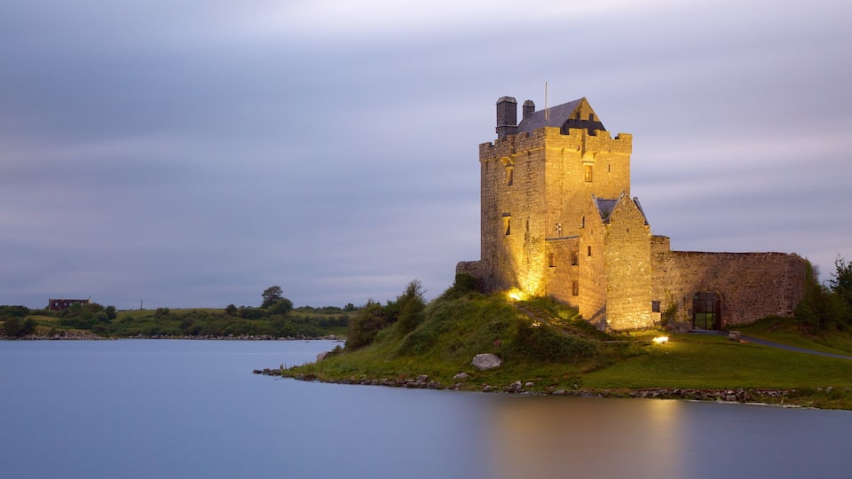 A castle on a grassy hill overlooking a calm lake.