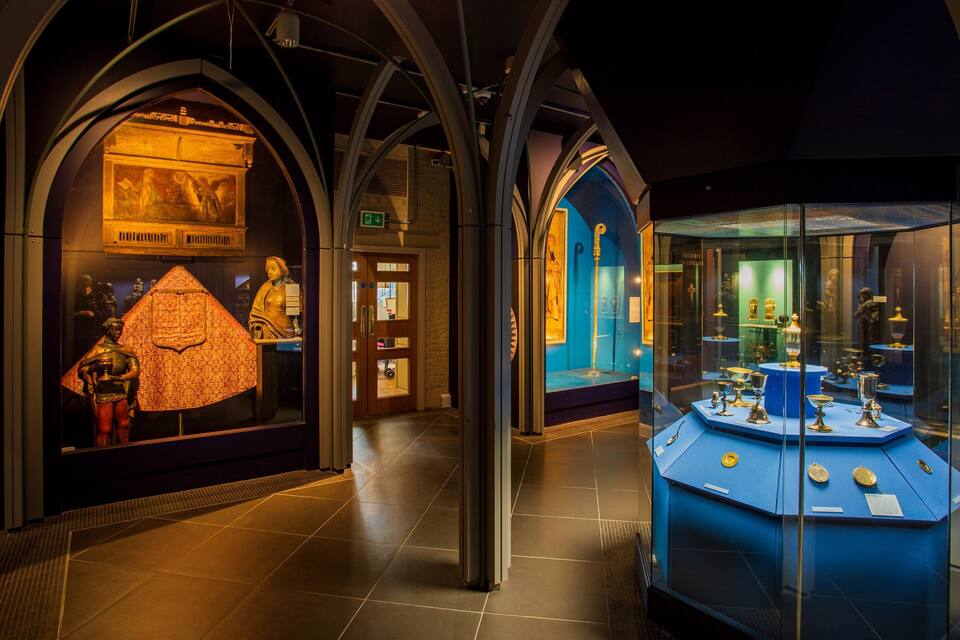A museum interior with gothic arches, a golden statue, and glass display cases with artifacts.
