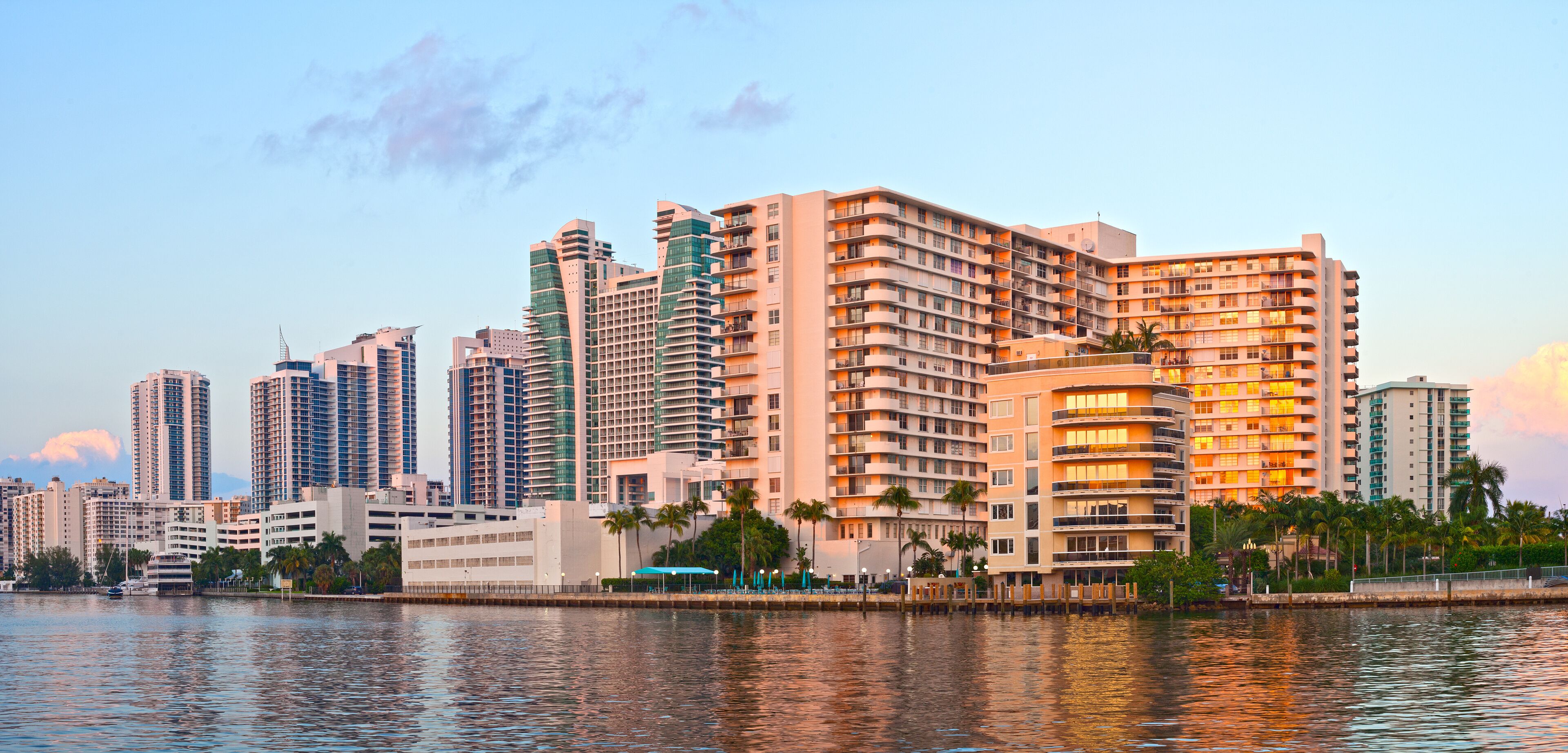 A waterfront cityscape with high-rise buildings and palm trees.