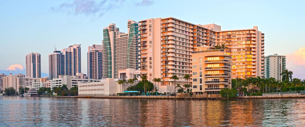 A waterfront cityscape with high-rise buildings and palm trees.
