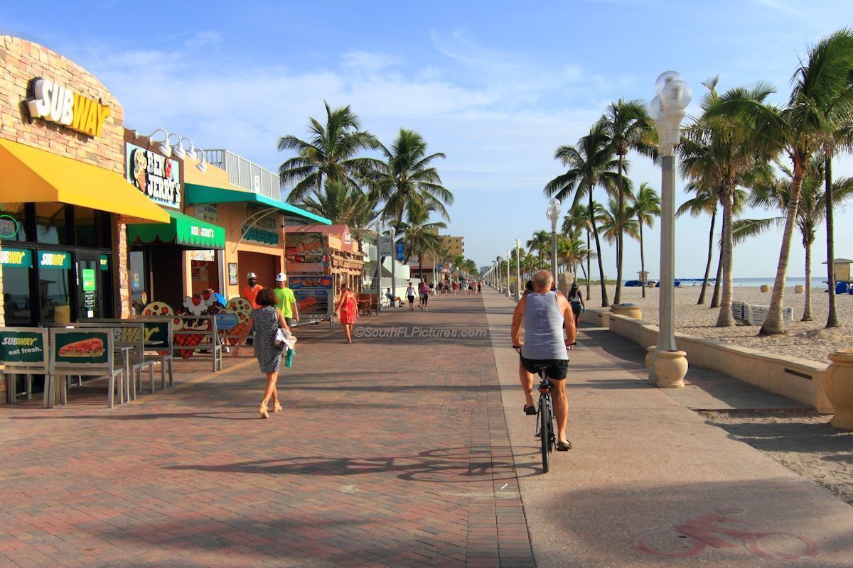 Un paseo marítimo con un restaurante Subway, palmeras y un ciclista.