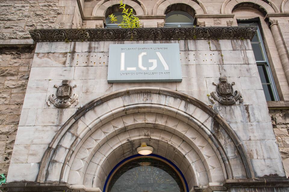 La entrada de la Galería de Arte de Limerick, con un ornamentado arco de piedra y una placa con el nombre de la galería.