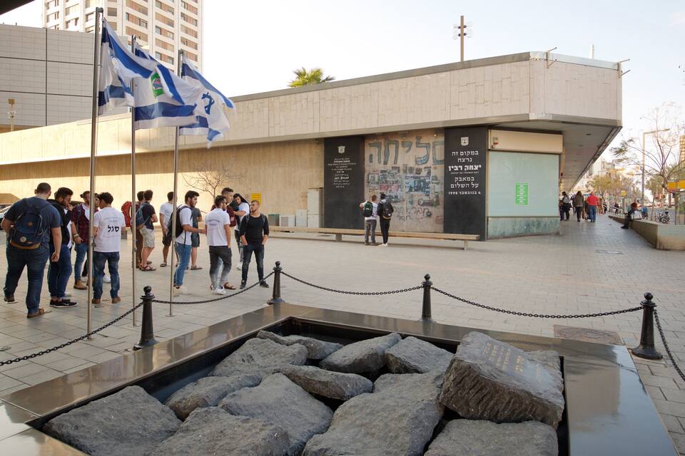Un groupe de personnes se tient devant un bâtiment orné d’une grande enseigne et d’un drapeau.