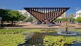 Une sculpture moderne dans une place publique, avec une fontaine et des nénuphars dans un bassin.