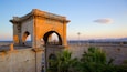A stone archway with graffiti, palm trees, and a sunset over the sea.