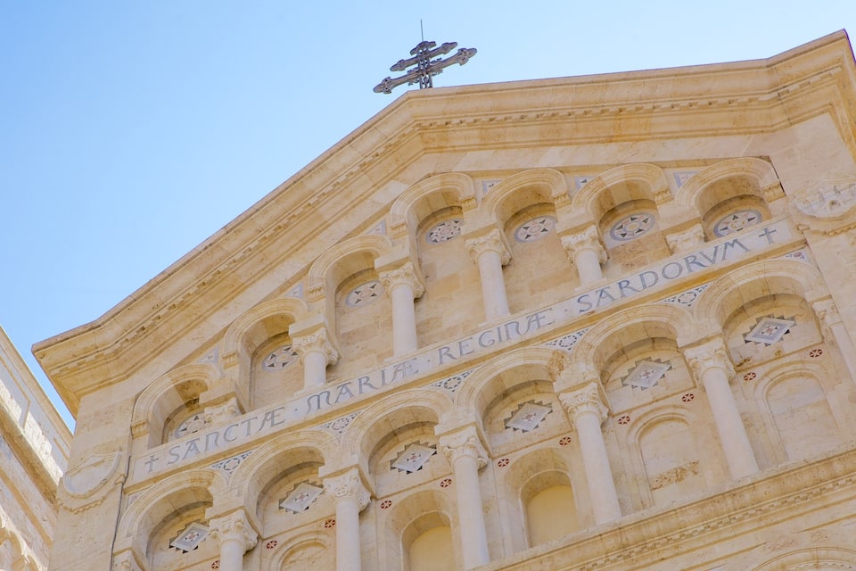 A building with arched windows and inscriptions, including "Maria Regina Sarda" and a cross symbol.