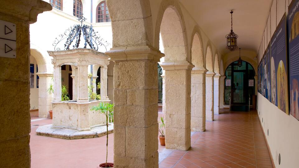 A historic building with arched corridors, stone columns, and a fountain.