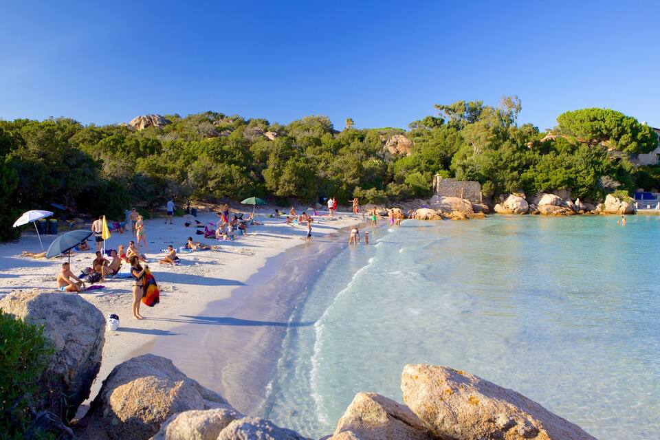 A beach with clear turquoise water, people sunbathing, and rocky outcrops.