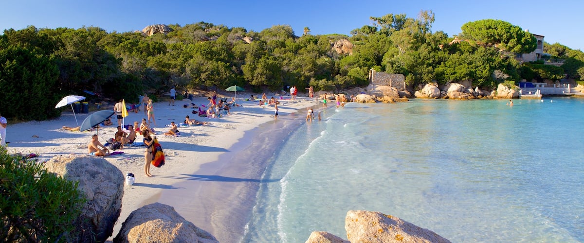 A beach with clear turquoise water, people sunbathing, and rocky outcrops.