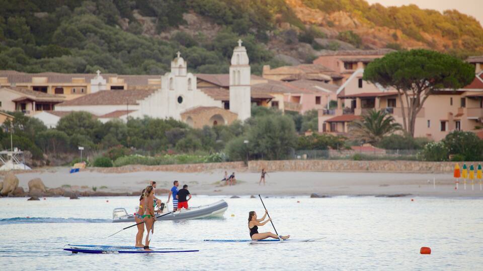 A coastal scene with paddleboarders, a boat, and a church in the background.