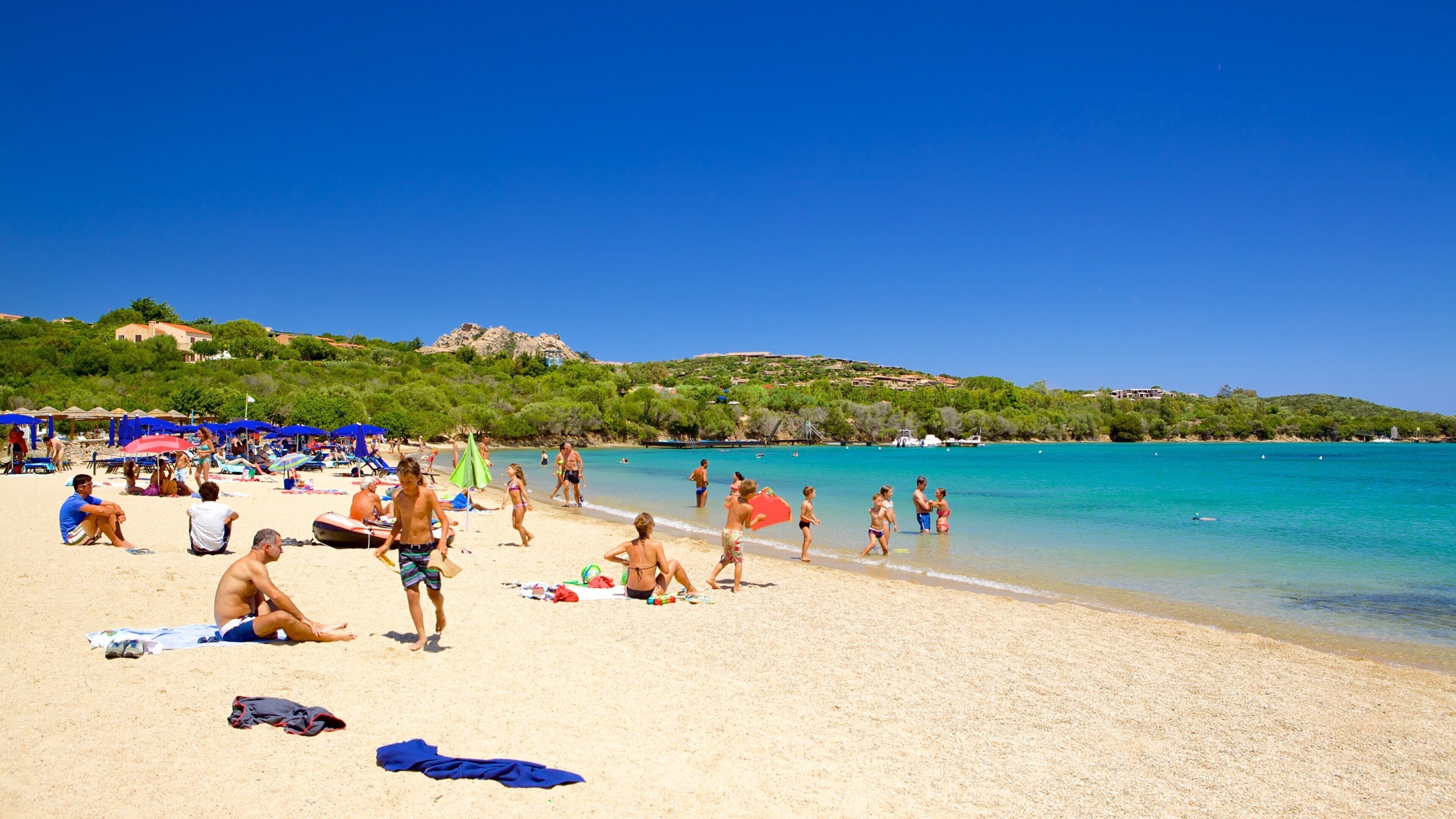 A sunny beach with people sunbathing, swimming, and playing.