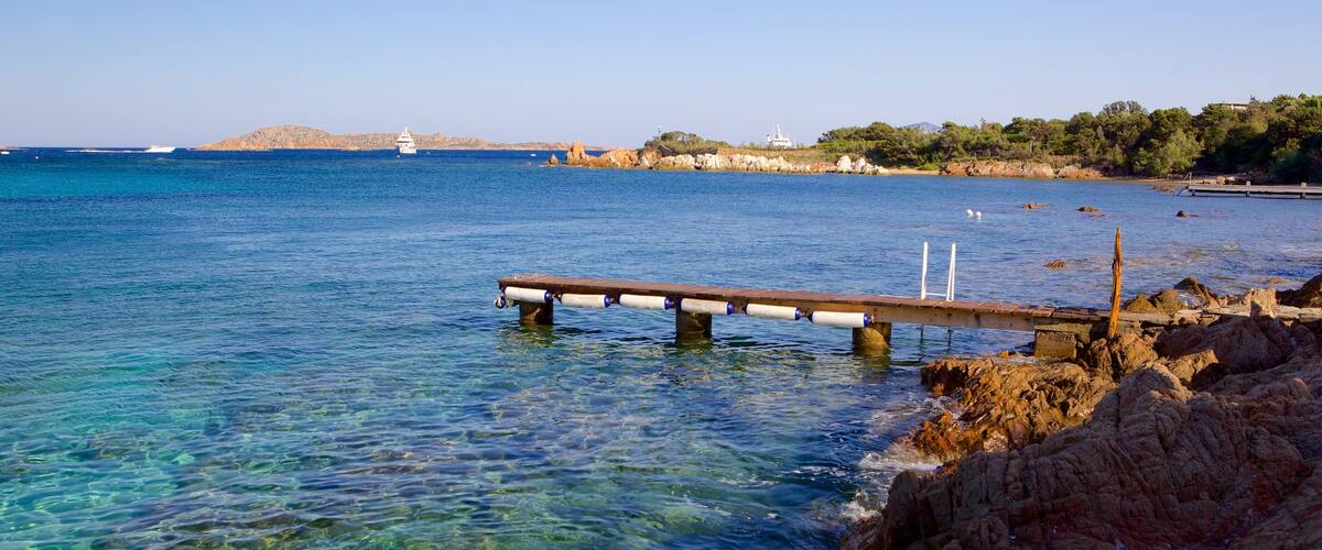 A rocky shoreline with a wooden pier extending into clear blue waters.