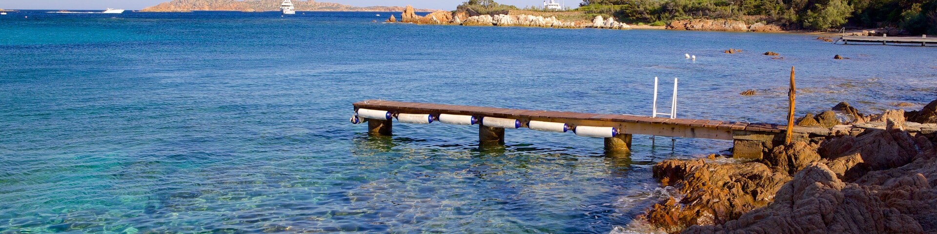 A rocky shoreline with a wooden pier extending into clear blue waters.