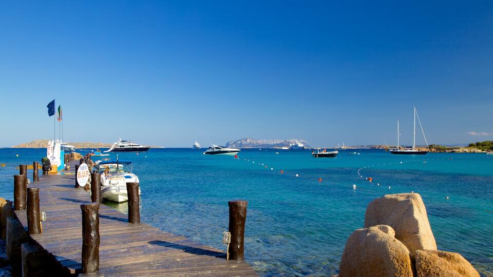 A marina with boats docked, a wooden pier, and a clear blue sea.