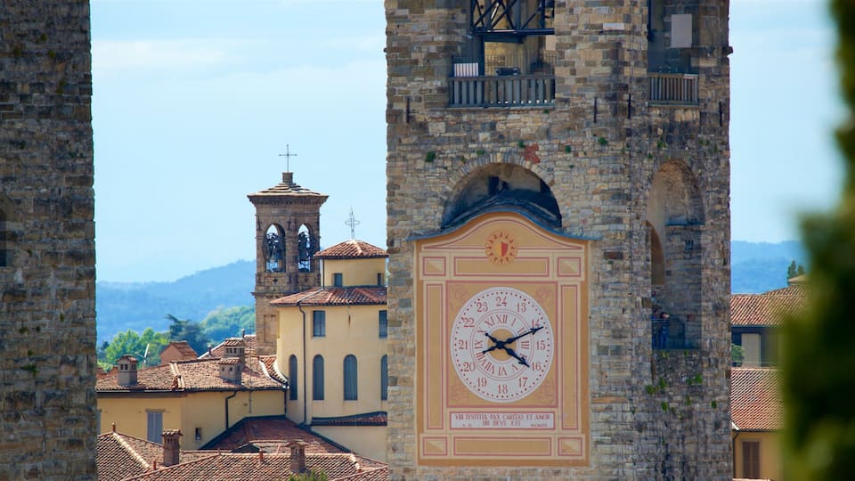 A historic clock tower with a large clock face, surrounded by stone buildings and a clear sky.