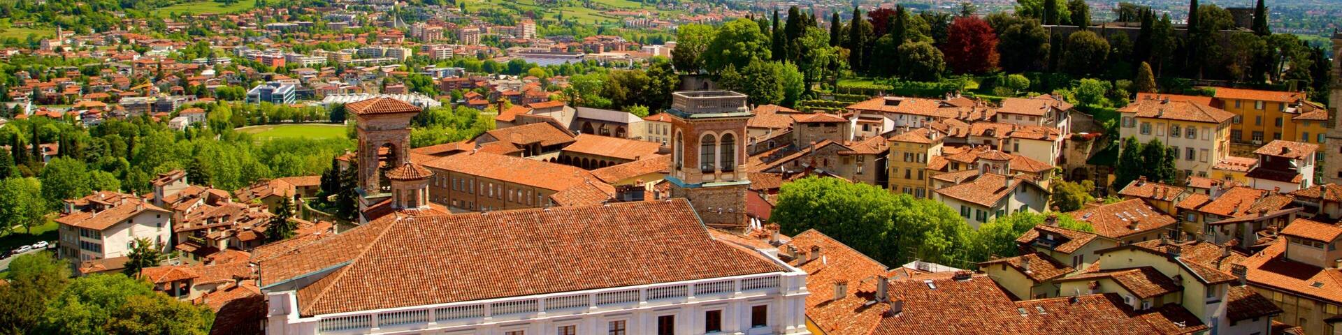 A historic town with terracotta-roofed buildings, a prominent white building with arches, and lush green hills in the background.