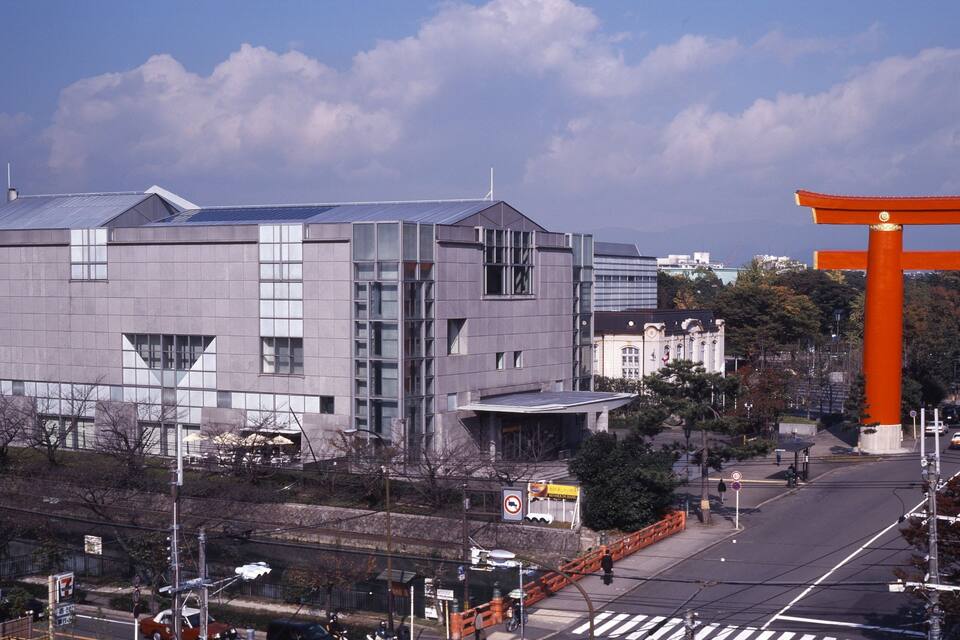 Um edifício moderno com um telhado de painéis solares, um tradicional portão torii vermelho e um céu azul límpido.